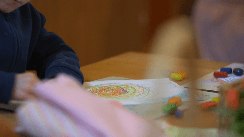 Ein Kind malt am Tisch mit Wachsmalfarben